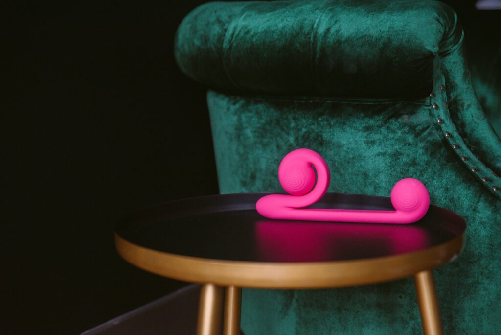 The Snail Vibe sits on an end table in front of an emerald green couch. The bright pink stands out against the dark green. For my Snail Vibe review article.