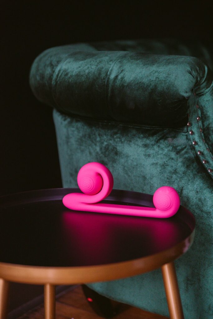 The Snail Vibe sits on an end table in front of an emerald green couch. The bright pink stands out against the dark green. For my Snail Vibe review article.