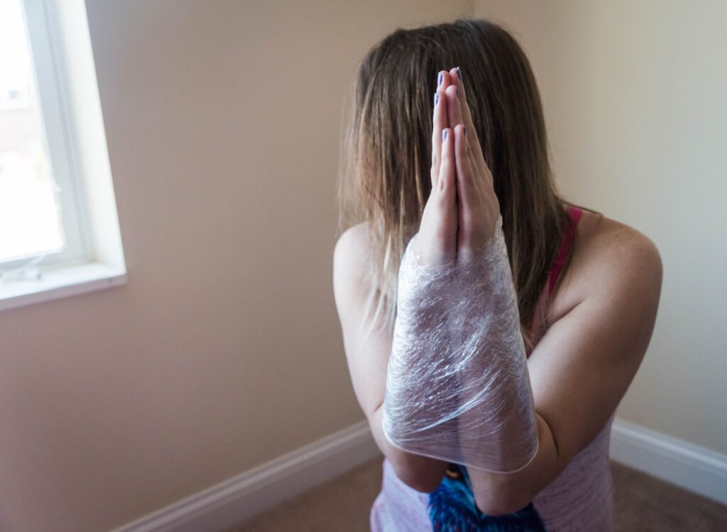 A person's forearms are secured together, fully touching throughout the forearms, as cling wrap is wrapped around the two of the arms, forcing them together in a "praying" motion. 