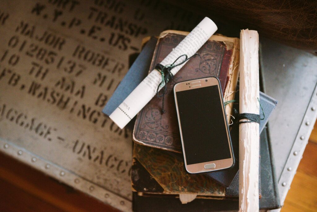 A cell phone sits out on a stack of books. The image has a yellow, aged hue that makes the juxtaposition between the shiny, modern cell phone and the aged books even more drastic. For my BDSM Safe Calls article.