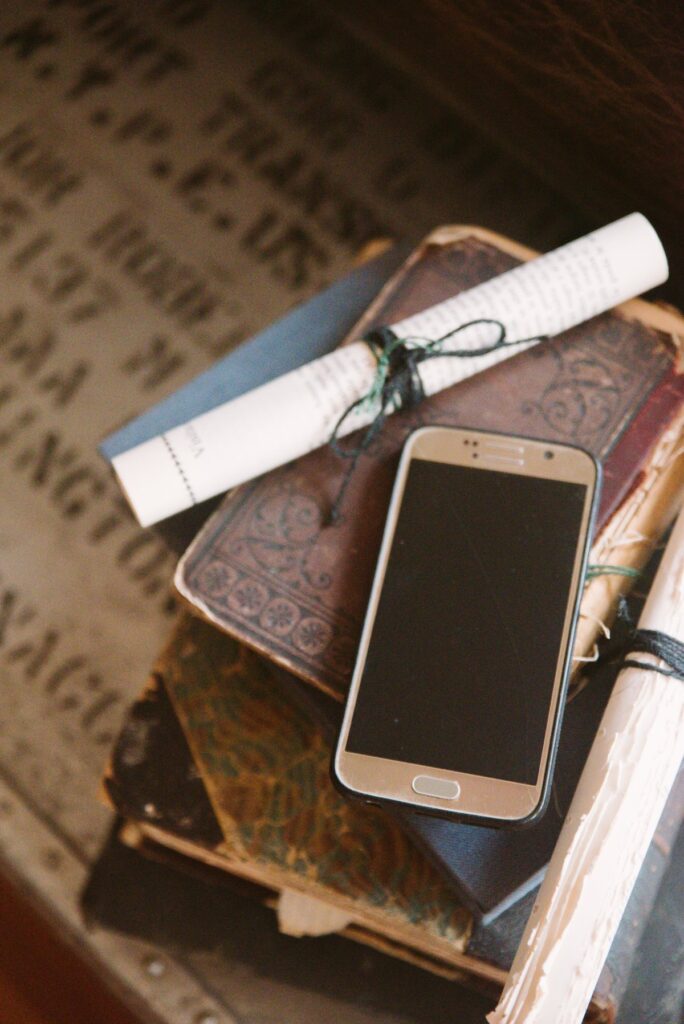 A cell phone sits out on a stack of books. The image has a yellow, aged hue that makes the juxtaposition between the shiny, modern cell phone and the aged books even more drastic. For my BDSM Safe Calls article.