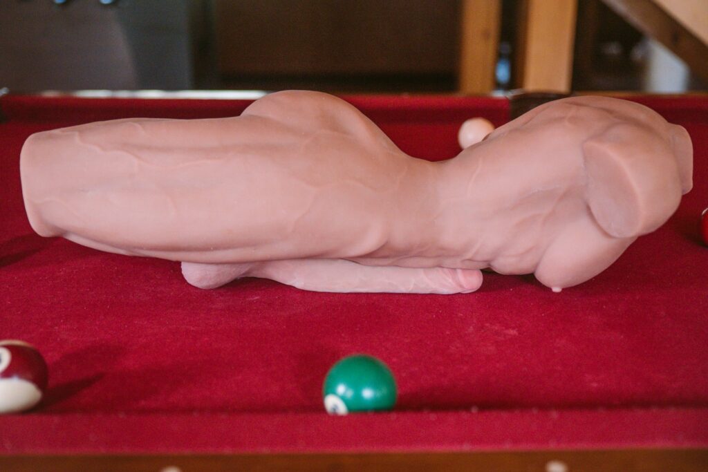 The sex doll lays, stomach-down, on top of a pool table. The huge, hard dildo is resting underneath of it, providing a "see-saw" of the weight dispersion of the sex doll. The doll is always off-center on the right or left when left "at rest". For my ppunson Jax male sex doll review.