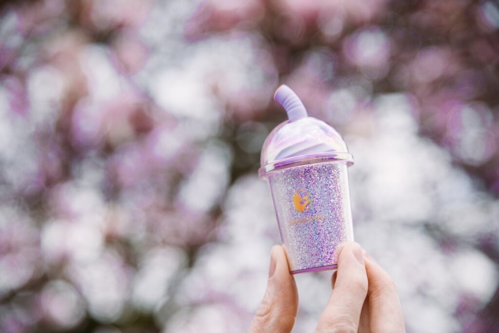 My hand holds the base of the vibrator in front of a cherry blossom tree. It looks very bright and playful. For my BeYourLover Joy Cup review.