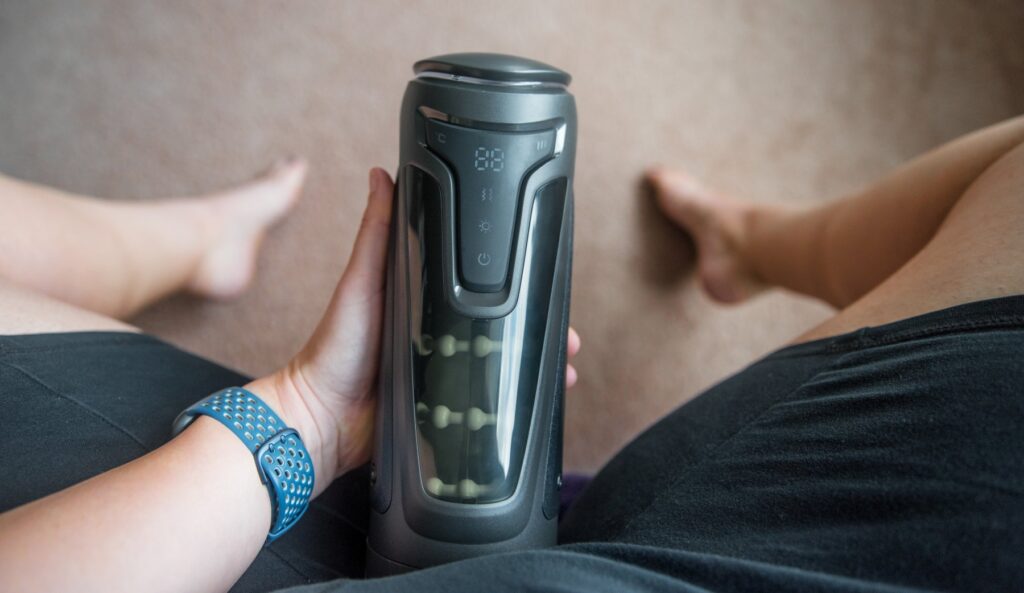 The Fleshy Thrust Sync shown between my legs. I'm using one hand to hold it. It can be sorta "propped" onto the penis to make it one handed use, but it's a larger stroker and may take two hands for some people. For my Fleshy Thrust Sync Review.