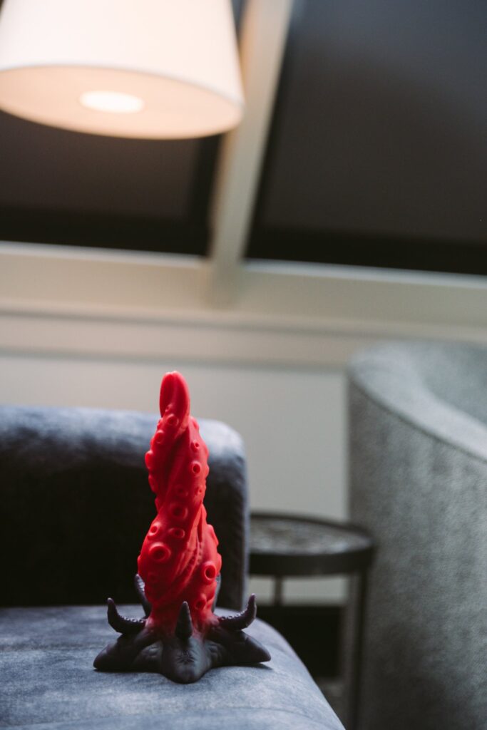 The Starfish dildo sits on a couch. The room is dark behind it, really highlighting the colors and unique shape of the dildo. For my Juliet Toys Starfish dildo review.