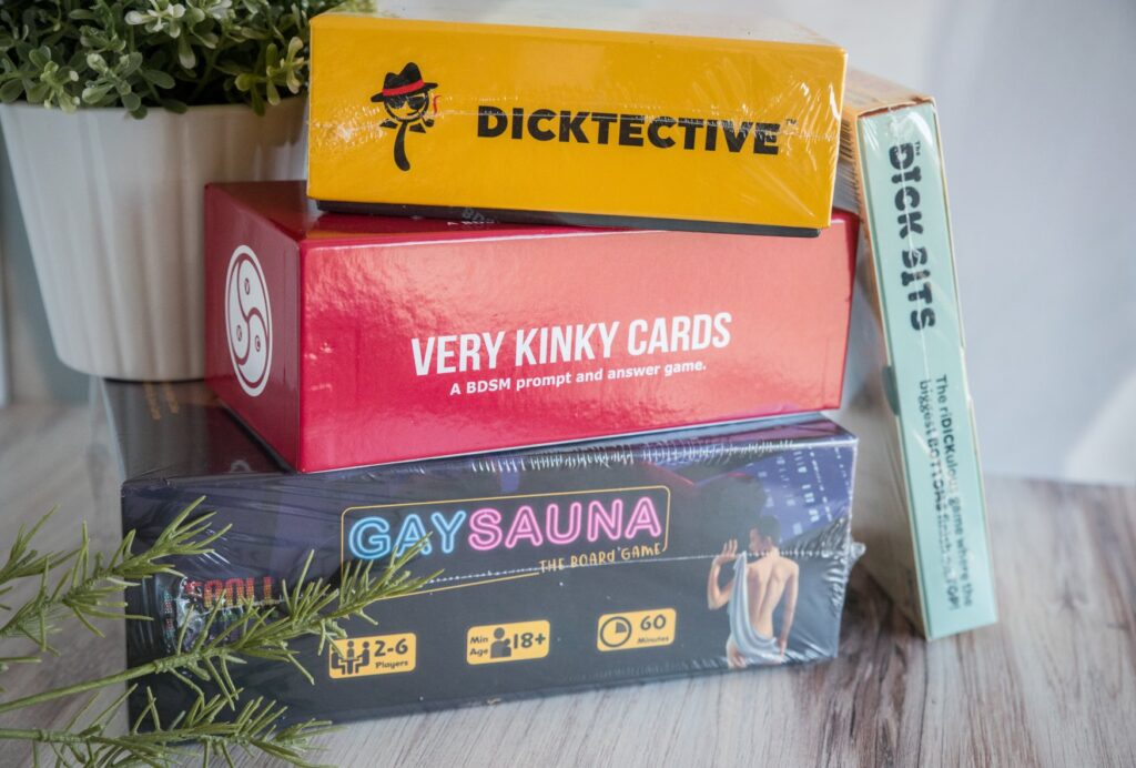 A stack of adult-theme board games are all stacked up. Some of them are still in the plastic wrap. For my article about kinky board games with friends that don't require sexual interaction.