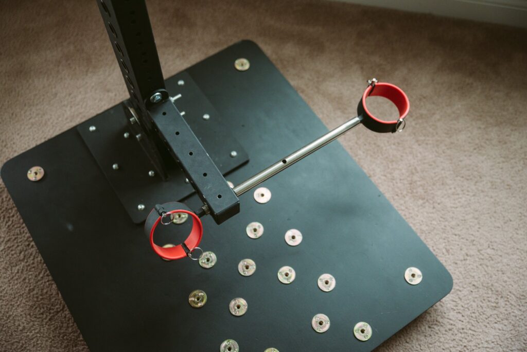 Close up of the ankle spreader bar attached to both ankle cuffs. This image, and its partner, showcase how the spreader bar can move freely within the spreader bar slot, allowing you to adjust exactly how far each ankle cuff is from the centerpoint but not adjust how far apart the two ankle cuffs are from one another.