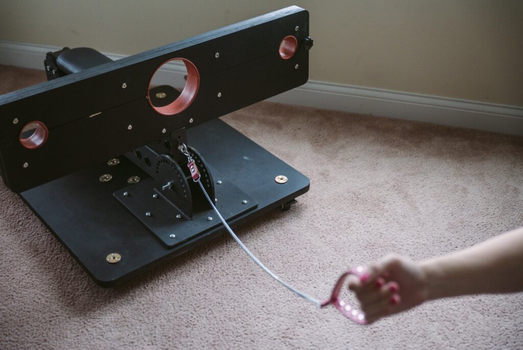My favorite way to use the sex furniture, as a small, kneeling platform with attached stockade. The L-shaped hinge is entirely folded up onto itself and resting directly on top of the platform. A hand holds a leash, attached to the eyebolt on the front of the furniture, showing how this could just be pulled along. For my Fetdom Multi-Position Floating Stockade Pillory Review.