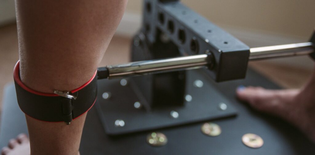 My partner's legs contained in the metal cuffs of the furniture. The sides of the cuffs look like they're pressing uncomfortably into their calf.