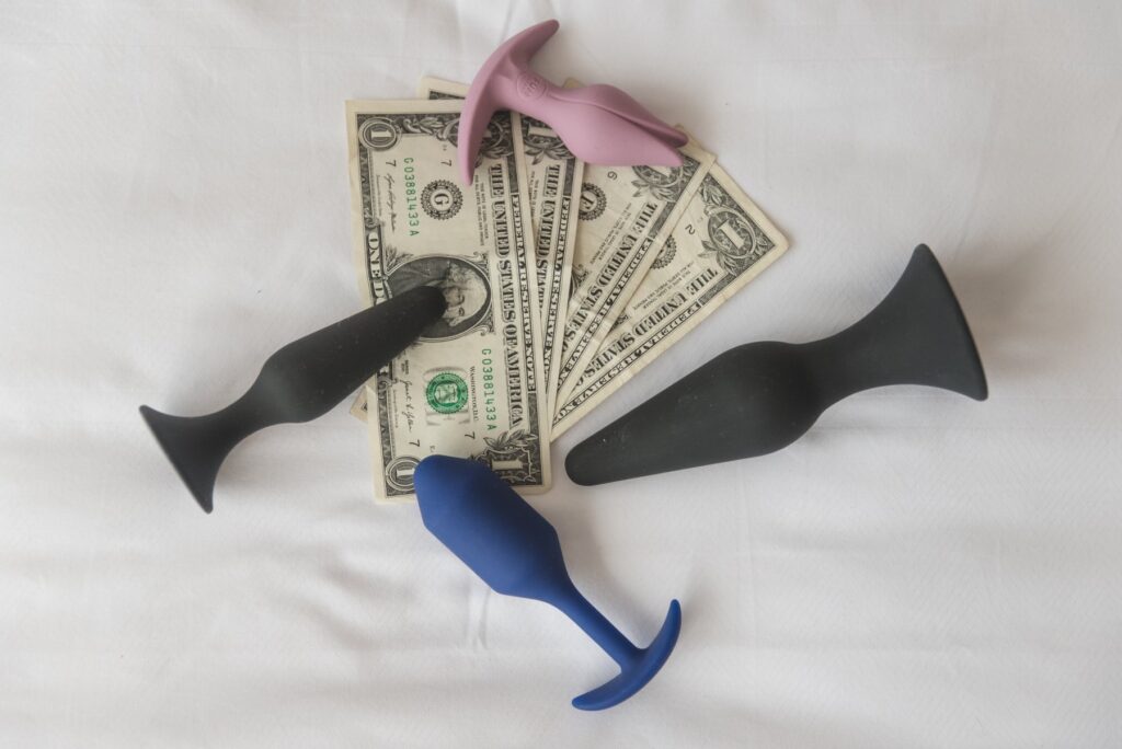 A pile of US dollar bills. Around the pile are 4 different anal toys. The anal toys are basic in design but quality. For my how to choose the best cheap sex toys article.