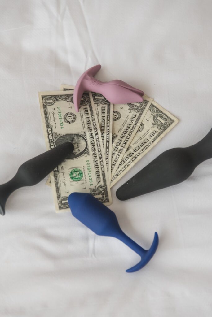 A pile of US dollar bills. Around the pile are 4 different anal toys. The anal toys are basic in design but quality. For my how to choose the best cheap sex toys article.