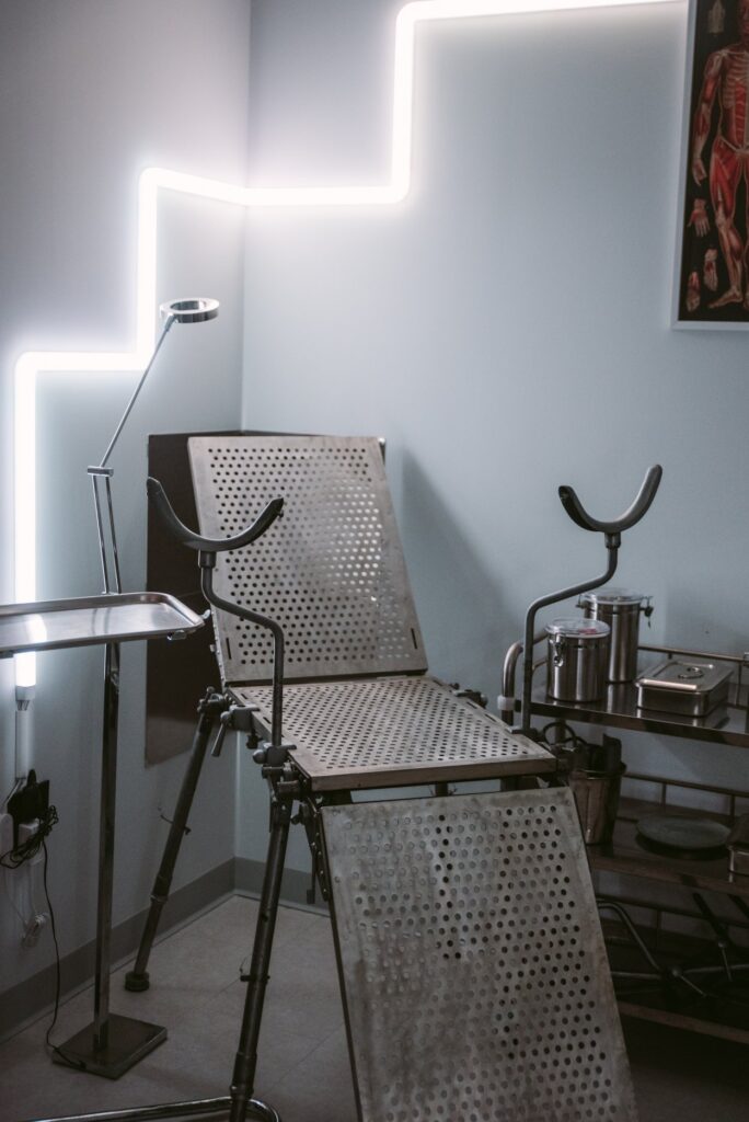 A medical fetish chair in a corner of the room. The chair is surrounded by medical fetish kink accessories. For my Medical fetish Ideas that Don't Break the Bank article.
