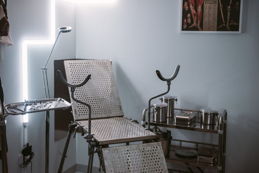 A medical fetish chair in a corner of the room. The chair is surrounded by medical fetish kink accessories. For my Medical fetish Ideas that Don't Break the Bank article.