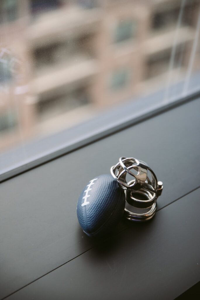 A small football-shaped stress ball sits out next to a metal chastity cage. For my femdom football scenes article.