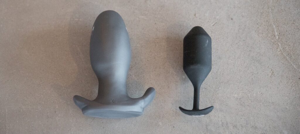 Two butt plugs shown side by side. One has an extra-thick butt plug retention area while the other has a super-slender retention area.
