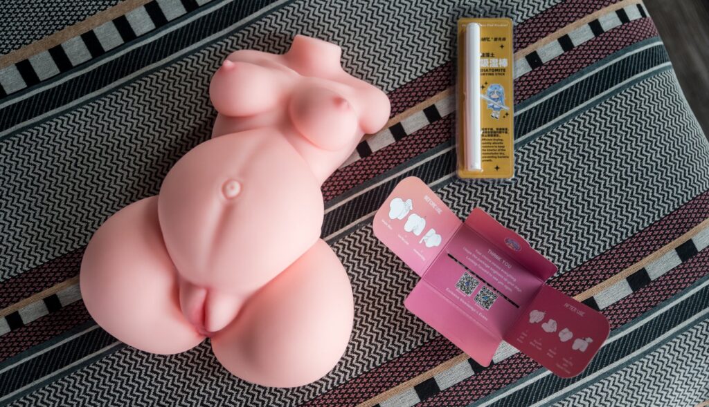 The Marissa sex doll laying out on the bed. The instructions and the drying stick it comes with are laying out next to it. For my MRLSexDoll Marissa review.