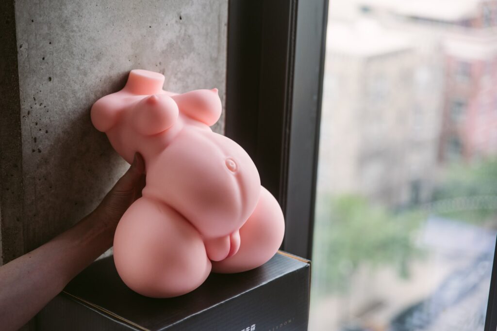 The Marissa sex doll leans up against a wall next to an open window. A hand helps prop the doll up, and the breasts have a teardrop shape to them. For my MRLSexDoll Marissa review.