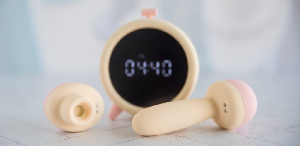 Both of the toys are removed from the top of the alarm clock and sitting out next to it. The alarm clock is on, displaying the time, in the background.