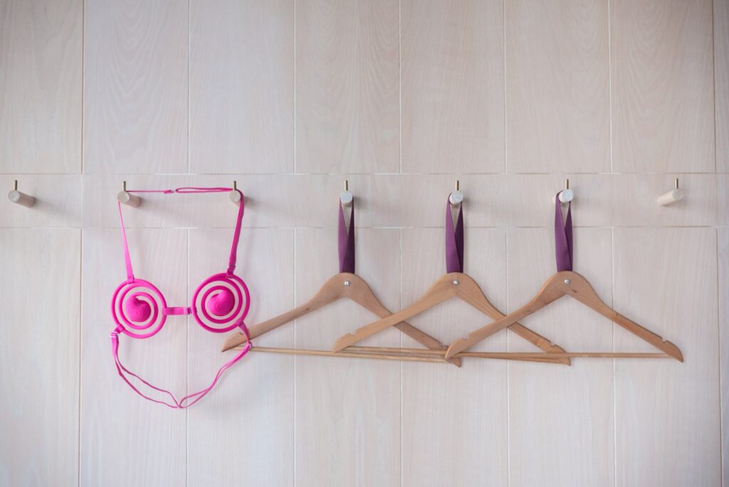 The Vkini hangs up on a clean, white wall, next to other hangers. It is very vibrant and pink. For my VVD Vkini review.