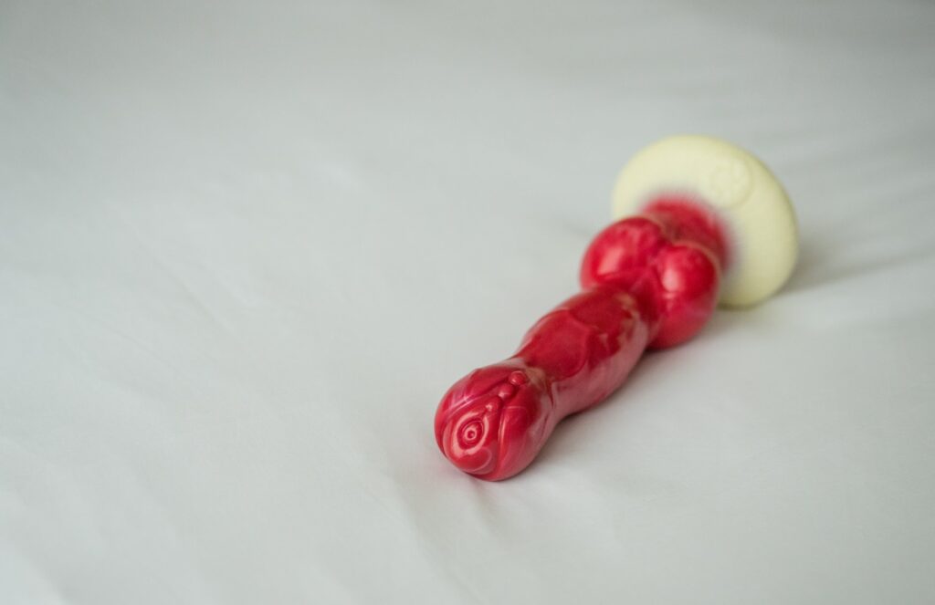The Juliet Toys PupJoy sits on top of a white bedspread. It looks shiny, very red, and very veiny.