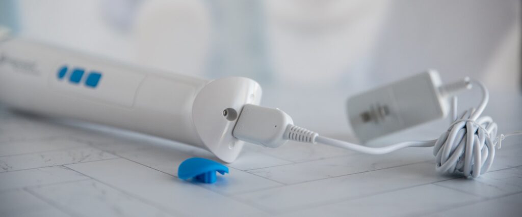 A close-up on the base of the Magic Wand Waterproof. The "waterproof" cap is removed, showcasing how it fully removes from the base of the wand. The charging cord is plugged into the base of the wand. For my Magic Wand Waterproof review.