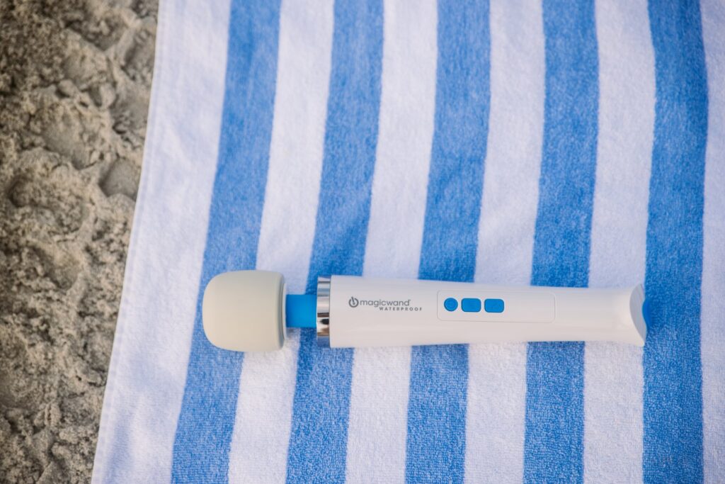 The Magic Wand laying on a striped beach towel on top of the beach sand. For my Magic Wand Waterproof review.