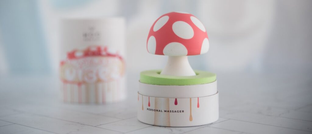 Packaging of the Mushroom Vibez sex toy. The lid is removed, showing the mushroom vibrator "popping up" in a sea of green that makes up its interior padding.