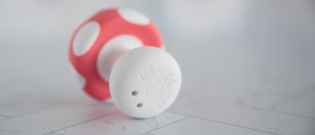 The Mushroom Vibez toy lays on its side. The bottom of the toy has a single button in the middle as well as two metal, magnetic charging port spots. For my Mushroom Vibez review.