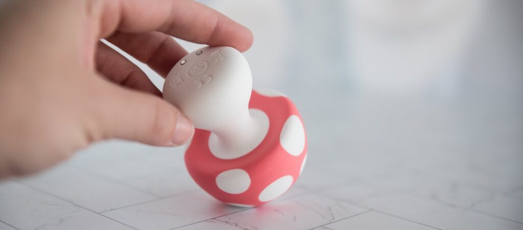 My fingers hold the vibrator. The head is pressed up against a flat surface, showcasing how the underside of the mushroom "cap" head is completely flat. For my Mushroom Vibez review.