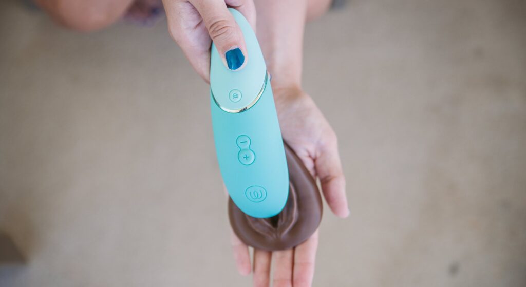 A person holds a vulva in their hands. They have positioned the Womanizer Next, an air suction vibrator, parrellel to the clit, enveloping the clit in the tip of the toy. For my How to Use a Clit Suction Toy article.