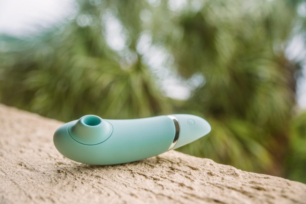 The Womanizer Next, air suction toy, lays out on a textured ledge, its air suction tip facing up towards the sky. For my How to Use a Clit Suction Toy article.