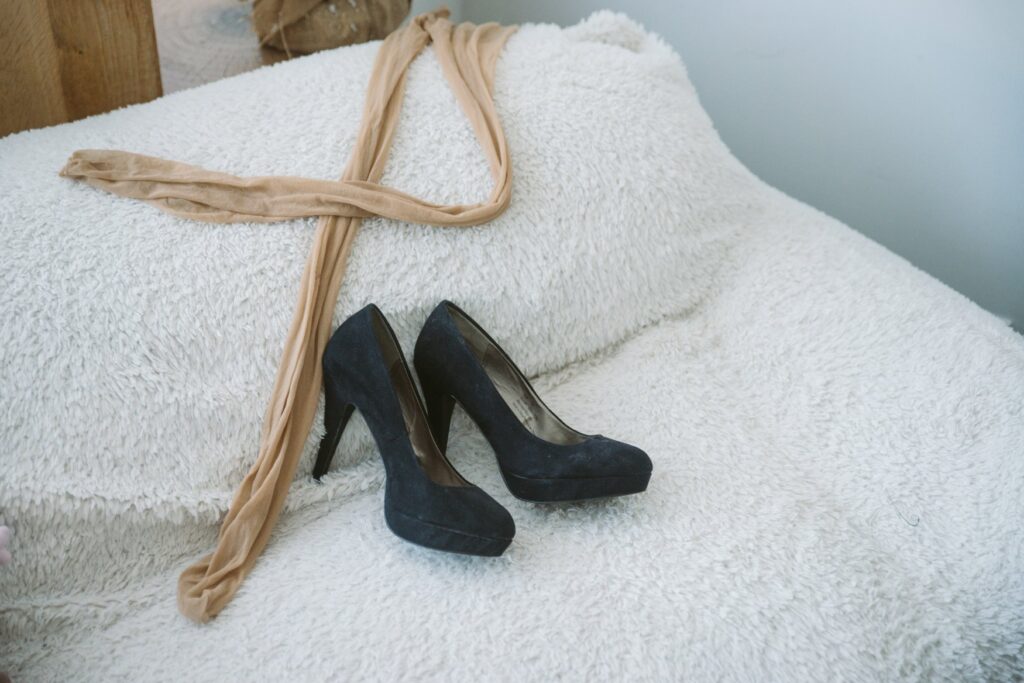 High heels and a pair of unworn pantyhose are laying out on a white, fluffy couch.