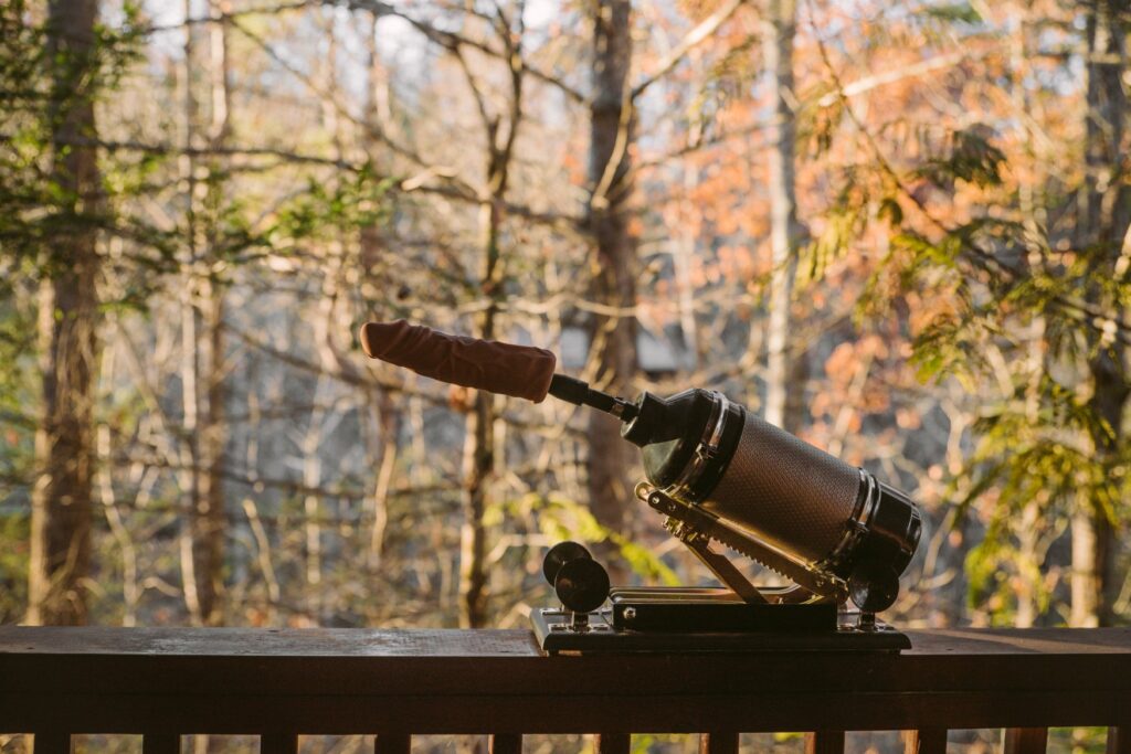 A sex machine sits out on top of a balcony ledge. The machine has a dildo on it. There are autumnal trees in the background. For my article about Are Sex Machines Worth It?