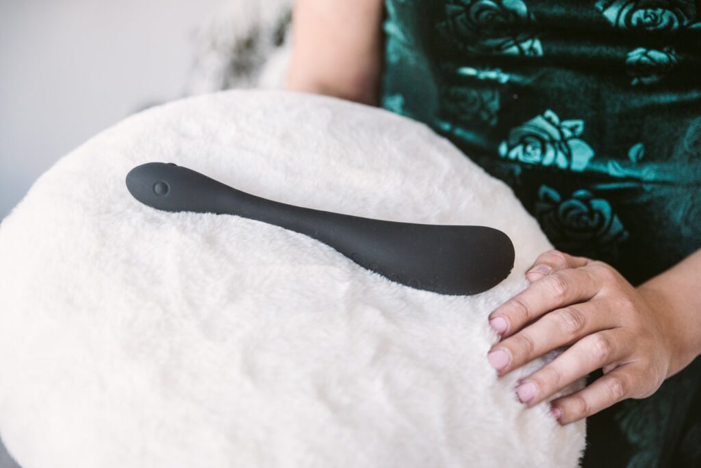 A person in a sequin green dress is holding a white, fluffy pillow. The black color of the AIRA stands out on the white fluffy pillow as the toy is presented to the camera. For my Honey Play Box AIRA review.