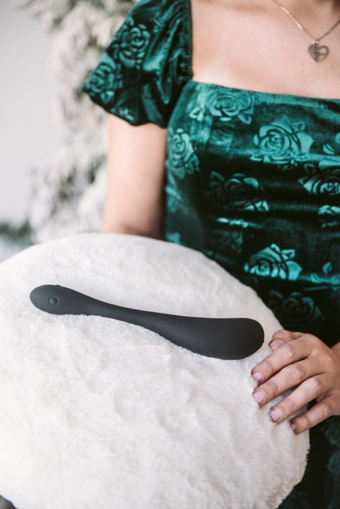 A person in a sequin green dress is holding a white, fluffy pillow. The black color of the AIRA stands out on the white fluffy pillow as the toy is presented to the camera. For my Honey Play Box AIRA review.