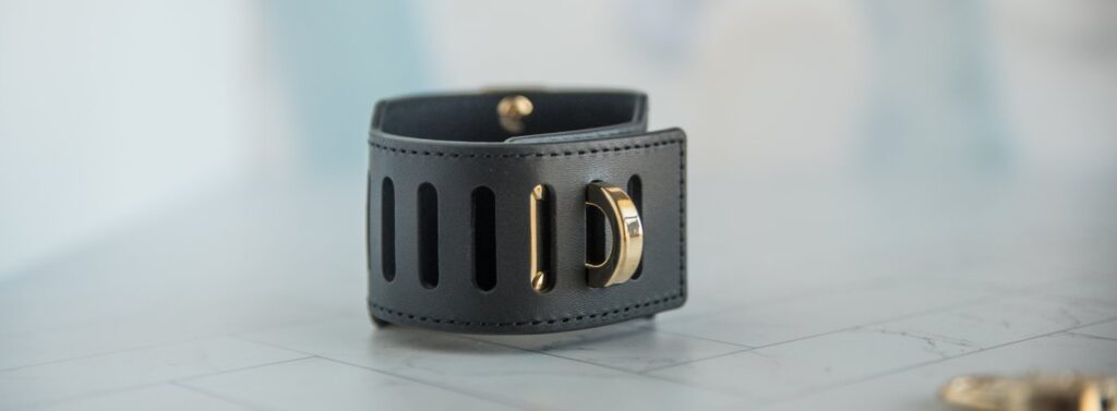 The cuff shown with the fastening post pushed through the hole to fasten the cuff shut. There is no lock attached, but this shows how the cuff fastens shut and could use a lock. For my Kink.com Gold Eclipse Wrist Cuff Set review.