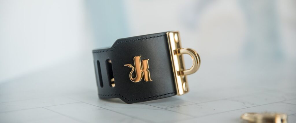 The cuff with the iconic Kink.com K emblem towards the camera. It's a nice, strong, shiny metal that color matches the rest of the hardware.