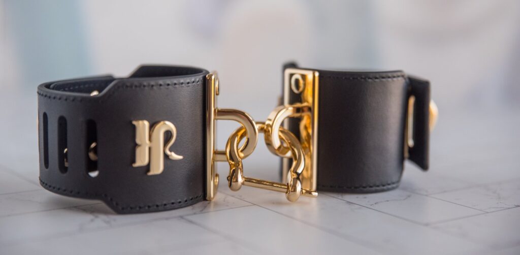 Close up on the fastener that goes between the two cuffs. The fastener is entirely closed up, fastening the two cuffs' D-rings together. For my Kink.com Gold Eclipse Wrist Cuff Set review.