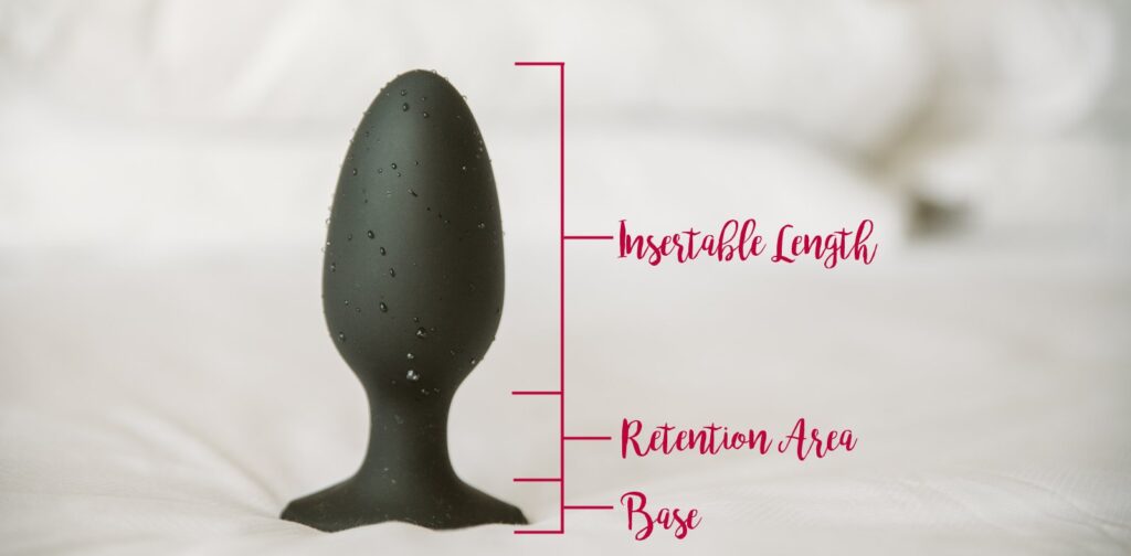 A photo of the Lovense Hush 2 butt plug sitting wet on a bed. Digital words showcase the insertable length, the retention area, and the base of the toy. For my best toys for anal stretching article.
