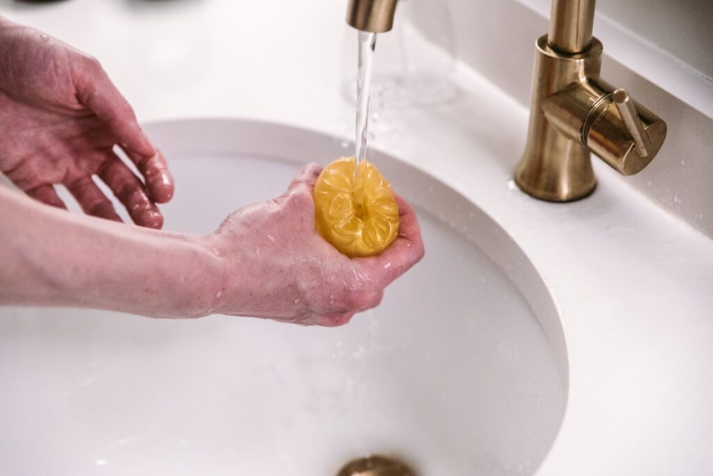 A stroker is held open underneath a sink spigot of running water.