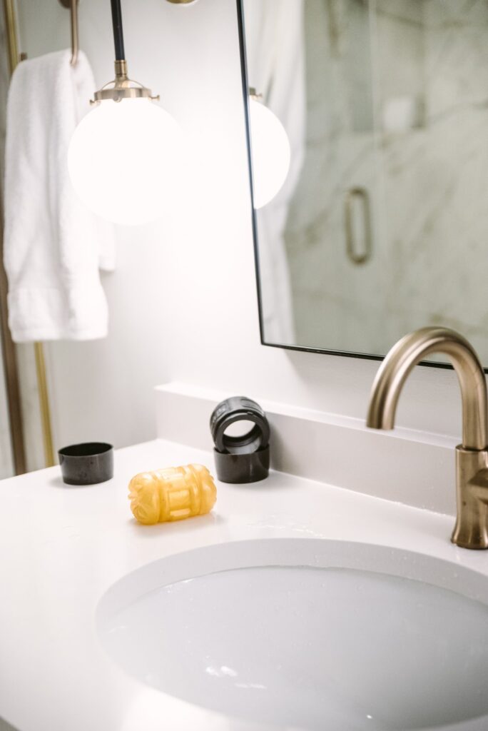 A penis stroker sits out on the side of a sink. The case of the sex toy is sitting nearby, but the stroker itself is sitting out by itself to allow the toy to dry.