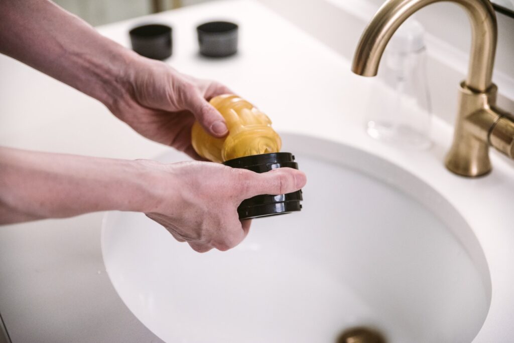 A Fleshlight Quickshot sex toy is shown hovering above a sink. The person is removing the soft, squishy interior of the stroker from the hard plastic shell that goes around the stroker. For my How to Clean a Pocket Pussy article.