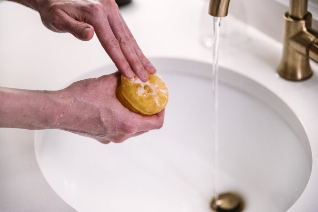 A stroker is held open underneath a sink spigot of running water. A hand really lathers the soap into the stroker, trying to make sure it gets into all of the small crevices. For my How to Clean a Pocket Pussy article.