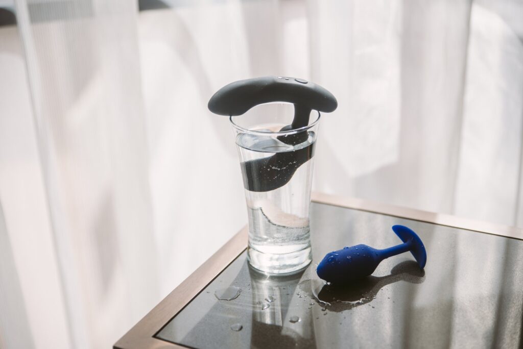 A prostate massager sitting in a glass full of water. Another butt plug sits next to the full glass of water. Image for my How to Clean the Ass Smell Off a Butt Plug.