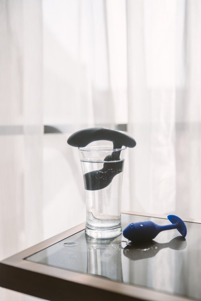 A prostate massager sitting in a glass full of water. Another butt plug sits next to the full glass of water. Image for my How to Clean the Ass Smell Off a Butt Plug.