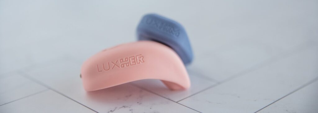 The LuxHer and LuxHim are resting against once another. The image closes up on the branding etched into the silicone sides of both items. For my Luxus review.