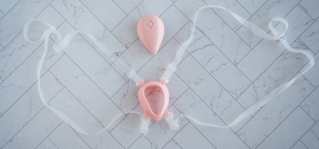 The Luxus vibrator harness laid out flat on a flat surface. The holster for the LuxHer is in the middle with both of the harness straps laid out on either side.