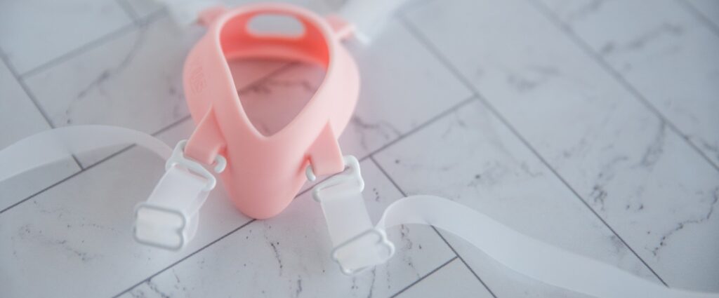 The Luxus vibrator harness laid out flat on a flat surface. There's a close-up of the slide-in strap fasteners that allow you to wrap the harness around each of the legs instead of stepping into the harness.