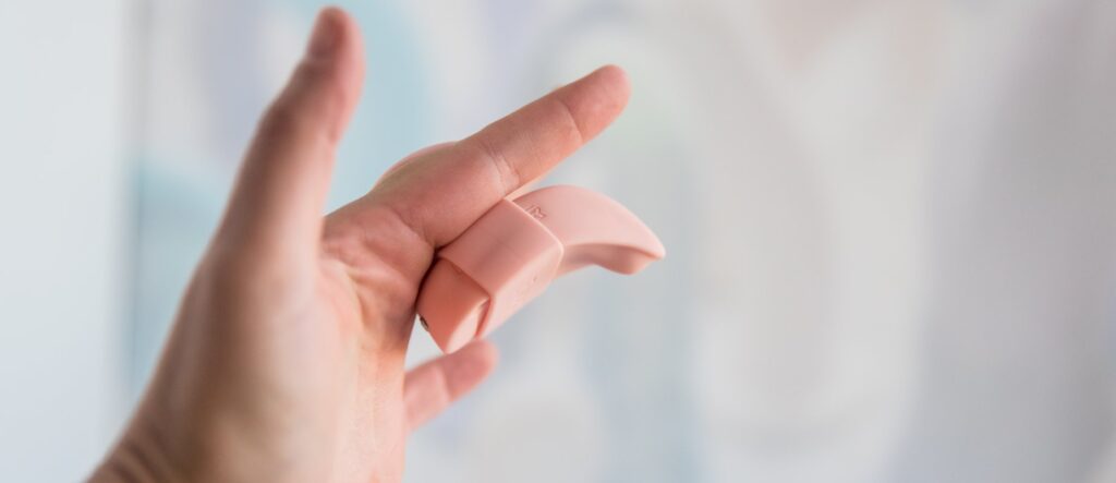 The LuxHer vibrator is in the Finger Grip holster. The Finger Grip is tucked in-between my pointer and middle fingers so it holds itself there and doesn't need to be held between my fingers. The vibrator's tip protrudes away from the toy to better nestle against the clit.