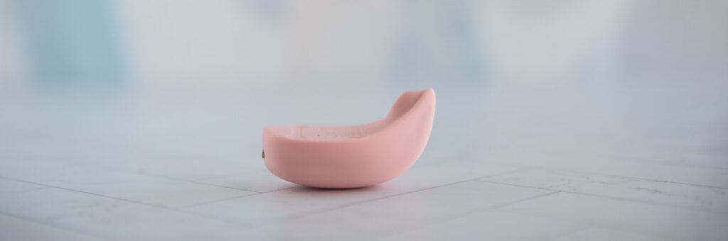 The LuxHer vibrator sits on a flat surface. The tip of the vibrator protrudes more than the flat surface of it, with a curvature designed to help wrap around the clitoris. For my Luxus review.